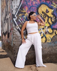 a woman in white pants leaning against a wall